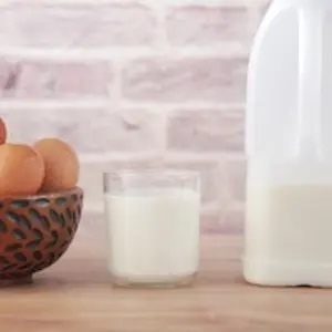 a bowl of brown eggs next to a short glass of milk and milk container